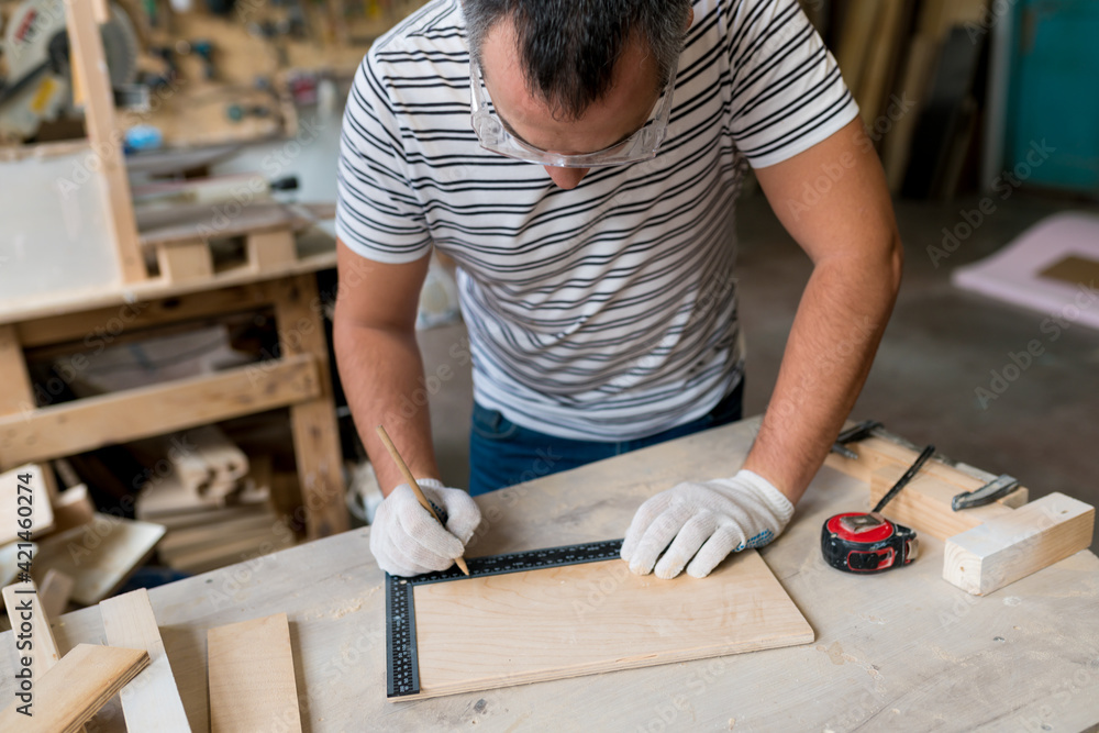 Close up of Man carpenter measuring a wooden board with a ruler with scale in workshop. Joinery work on the production and renovation of wooden furniture. Small Business Concept Close up of Man carpenter measuring a wooden board with a ruler with scale in workshop. Joinery work on the production and renovation of wooden furniture. Small Business Concept