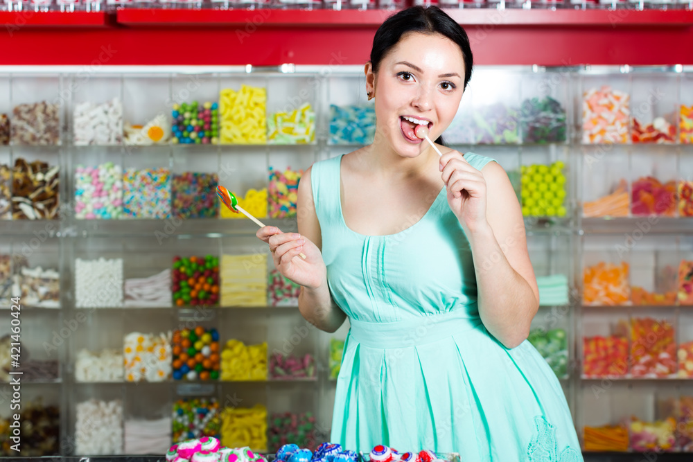 friendly girl posing in the store with lolly on the background of counters with sweets