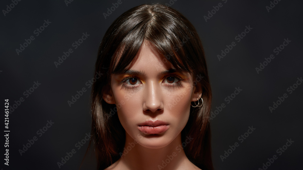 Fototapeta premium Beauty portrait of young brunette woman with brown eyes and colorful makeup looking at camera, posing isolated over black background