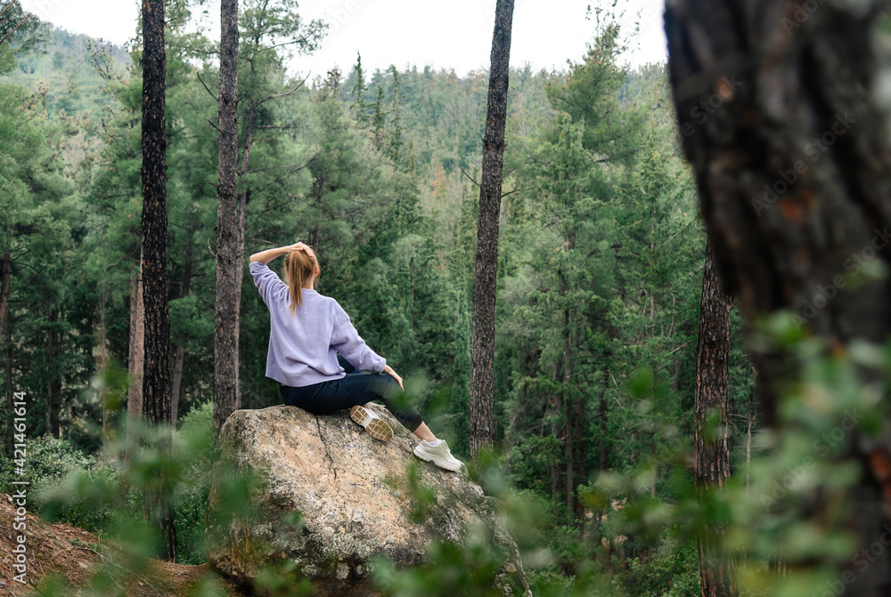 Dreamy young woman sitting on the big rock at forest Dreamy young woman sitting on the big rock at forest