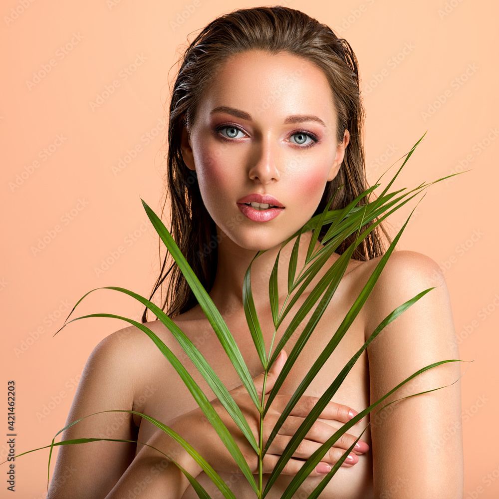 White woman with healthy skin of body and palm leaves. Tanned body of an attractive girl with green plants. Large palm leaves cover the breast. White woman with healthy skin of body and palm leaves. Tanned body of an attractive girl with green plants. Large palm leaves cover the breast.