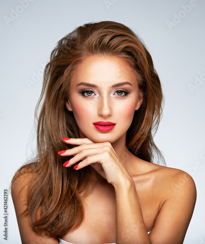 Face of young woman with red nails, lipstick and long brown hair. Model with fashion makeup.