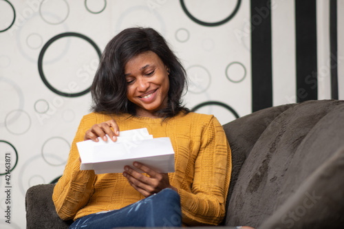 beautiful young black woman smiling while opening a letter to read