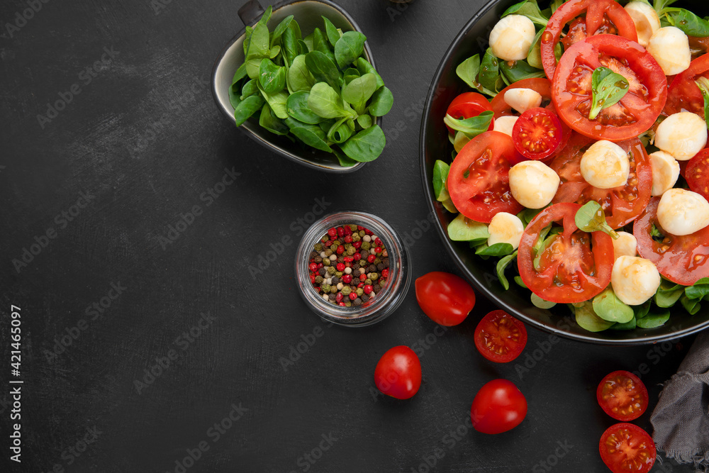 Delicious Italian caprese salad with sliced tomatoes and mozzarela on dark background.