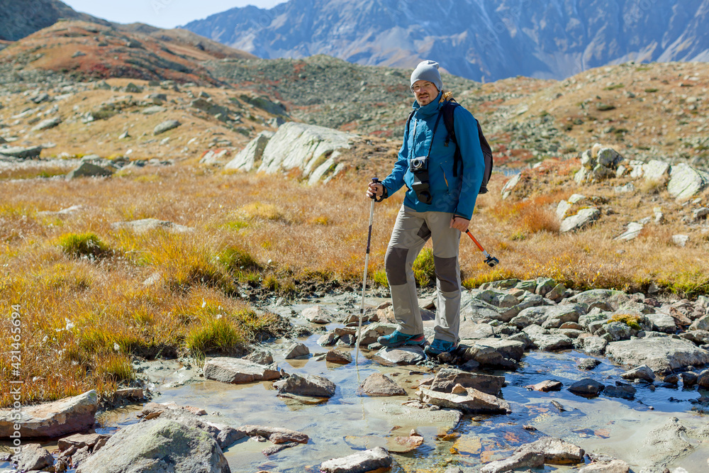 Obraz premium Hipster mountain blogger for lifestyle design. Adventure tourism. Trekking of young man vlogger with camera. Solo tourist in the Alps. hoto with copy space
