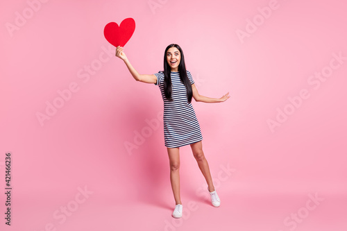 Full length body size view of pretty cheerful slender girl holding in hand heart flying enjoying isolated over pink pastel color background © deagreez