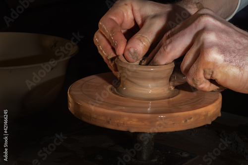 Potter at work. Potter's hands in clay form a pot on a circle. Light hands on dark background