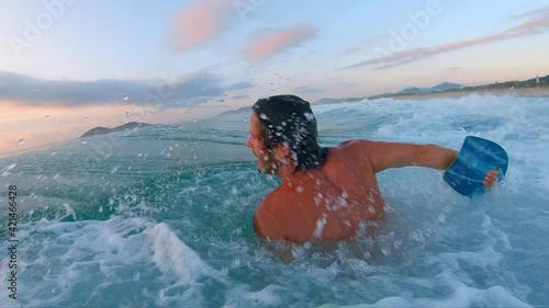 Sunrise bodyboarding. Young man appears from water and shakes his head after passing ocean. Surfer with handboard appears from the water photo