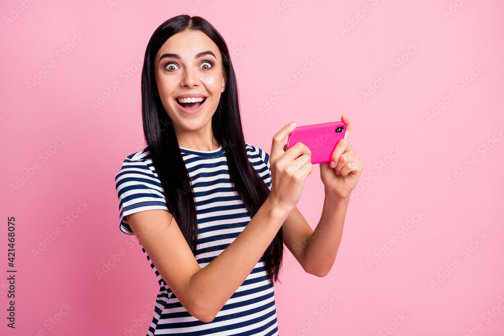 Photo portrait of amazed girl with open mouth holding phone in two hands vertically isolated on pastel pink colored background Photo portrait of amazed girl with open mouth holding phone in two hands vertically isolated on pastel pink colored background