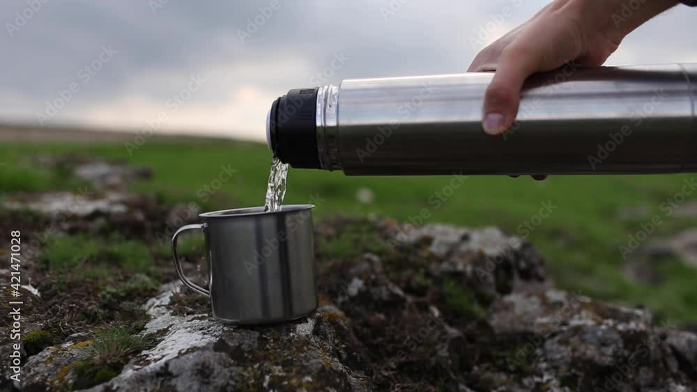 Close-up of male hand pouring water into the steel cup from thermos bottle in mountains on hiking. Close-up of male hand pouring water into the steel cup from thermos bottle in mountains on hiking.