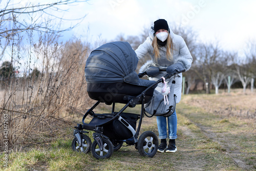 Young woman in medical mask walking with the baby stroller. Jogging in the park is good exercise during coronavirus epidemic.