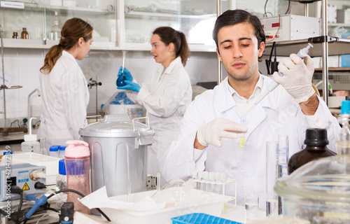 Canvastavla Intelligent student performing experiments in university laboratory, using mechanical lab pipette for mixing chemicals