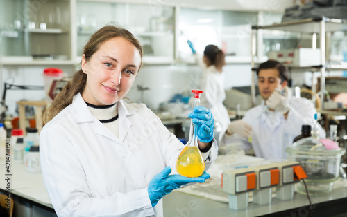 Professional female chemist working in laboratory, analyzing liquid samples in test flasks..