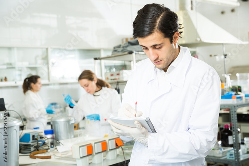 Student of Faculty of Biology performing experiments in university laboratory  writing results in workbook..