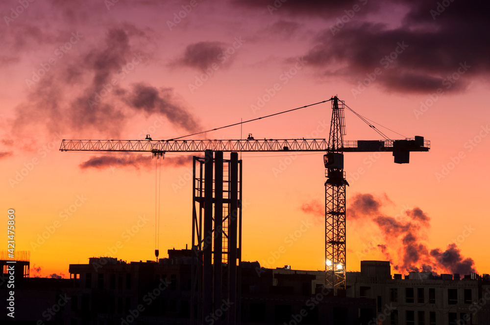 Silhouette of industrial construction tower crane against sunset orange and pink color sky on the background, real estate building development, architecture business concept work