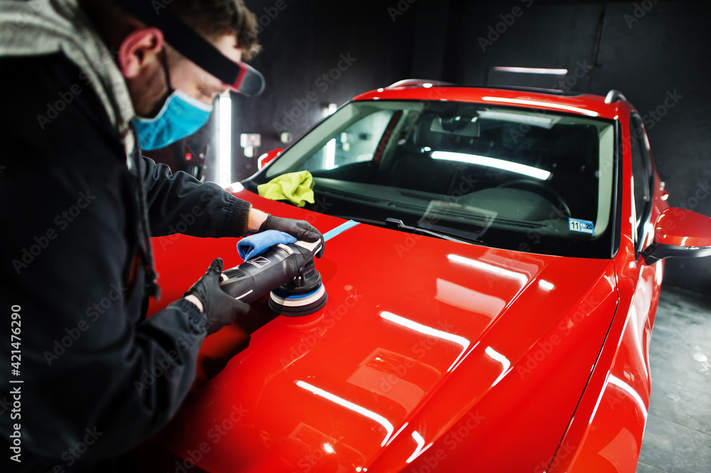 Car detailing concept. Man in face mask with orbital polisher in repair shop polishing orange suv car. Car detailing concept. Man in face mask with orbital polisher in repair shop polishing orange suv car.