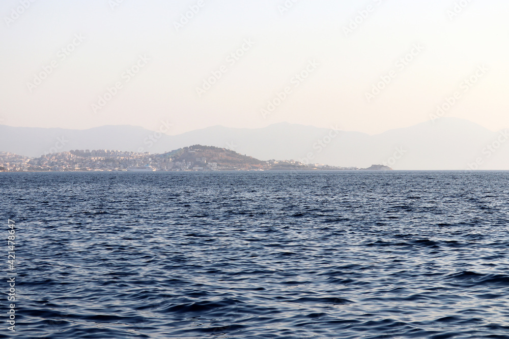 View from the blue sea to mountains and seaside town in mist. Beach vacation and travel concept