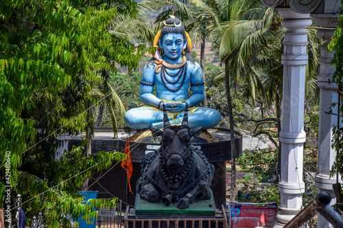 Front view of giant statue of lord shiva and his vehicle nandi bull under bright sunlight surrounded by green trees at kanheri math kolhapur city maharashtra India. focus on statue.