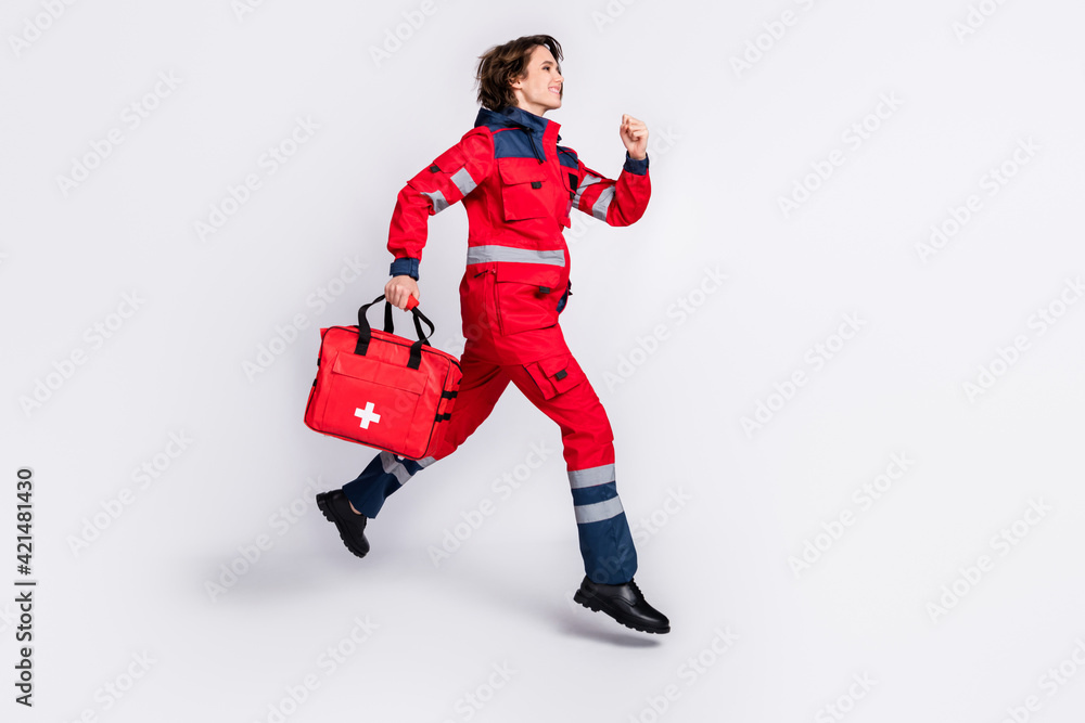 Full size profile side photo of happy smiling girl paramedic running in air first aid help isolated on grey color background Full size profile side photo of happy smiling girl paramedic running in air first aid help isolated on grey color background