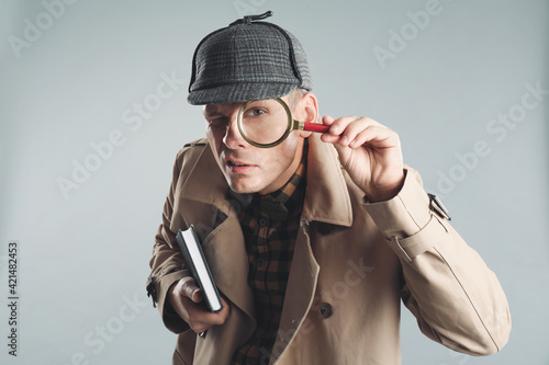 Male detective looking through magnifying glass on grey background photo