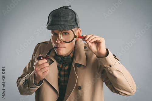 Billede på lærred Male detective with magnifying glass smoking pipe on grey background