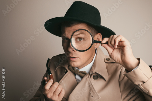 Male detective with smoking pipe looking through magnifying glass on beige background photo