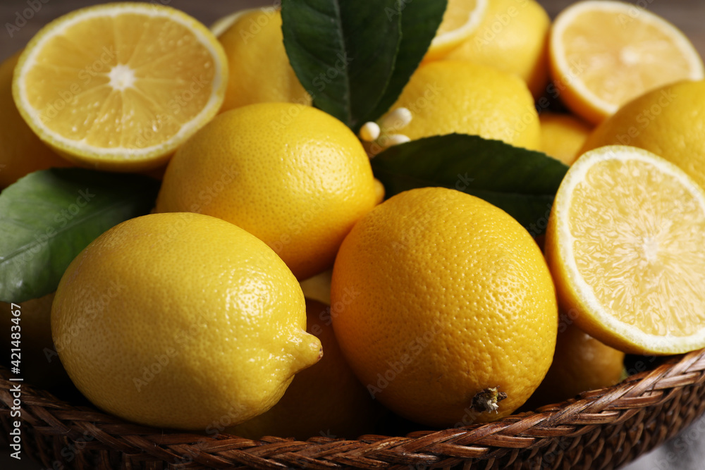 Many fresh ripe lemons in wicker bowl, closeup
