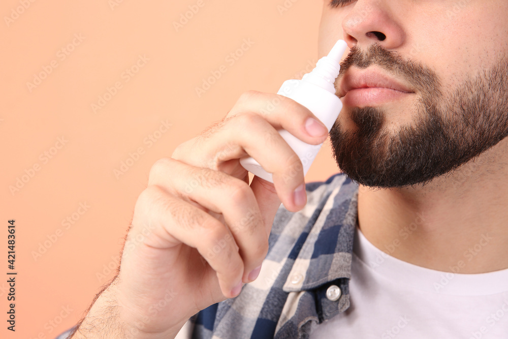 Man using nasal spray on peach background, closeup. Space for text Man using nasal spray on peach background, closeup. Space for text