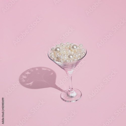 Martini cocktail glass with white pearls on pastel pink background. Retro fashion aesthetic idea. Romantic concept.