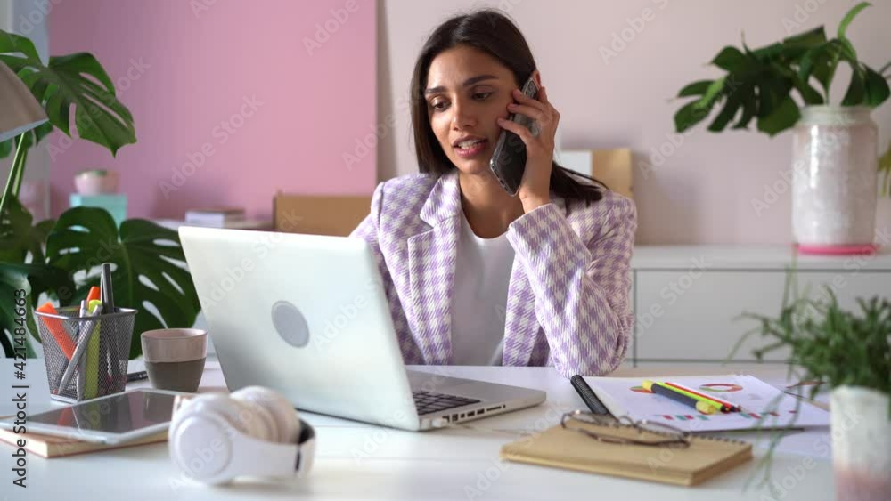Smiling young Indian mixed-race business woman professional talking on phone using laptop sit at office desk Smiling young Indian mixed-race business woman professional talking on phone using laptop sit at office desk
