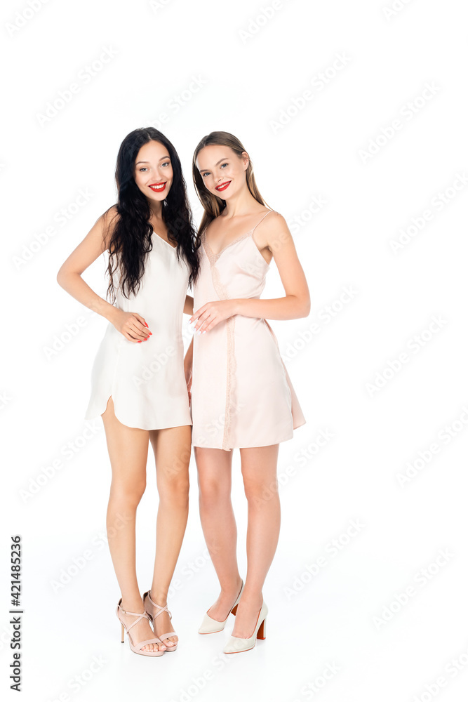 full length of happy women in dresses smiling while standing isolated on white full length of happy women in dresses smiling while standing isolated on white