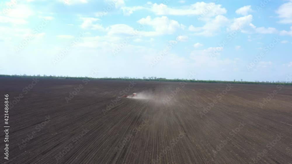 aerial view of tractor with the seeder working at the large field at the windy spring day
