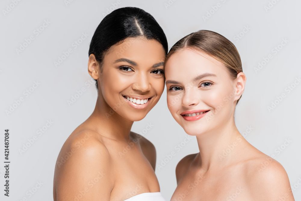 positive interracial women smiling while looking at camera isolated on grey positive interracial women smiling while looking at camera isolated on grey