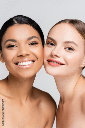 interracial women smiling while looking at camera isolated on grey
