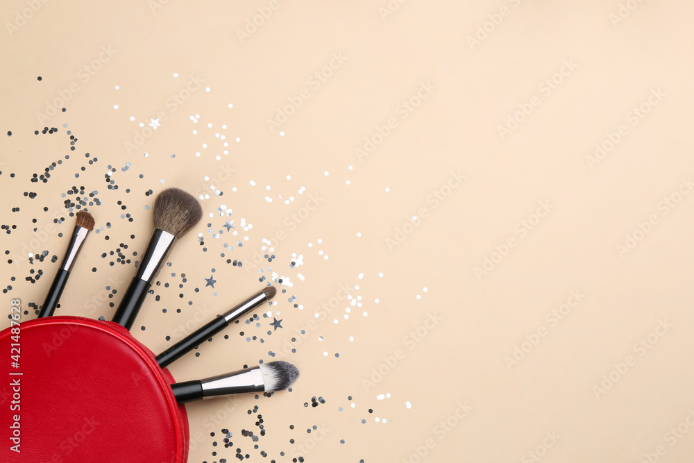 Different makeup brushes, case and shiny confetti on beige background, flat lay. Space for text Different makeup brushes, case and shiny confetti on beige background, flat lay. Space for text