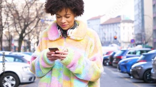 Young beautiful curly hair black woman outdoor in the city smiling using smartphone writing message, shoppinh online or home banking photo