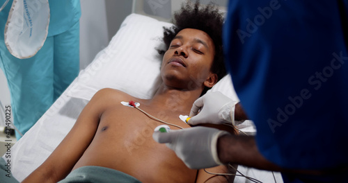 Doctors placing ecg electrodes on young unconscious afro-american patient photo