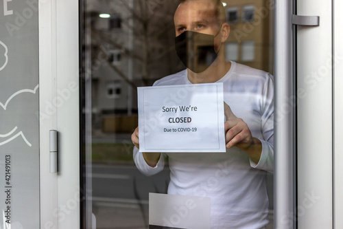 Man with protective face mask closing business activity due to covid-19 emergency lockdown quarantine. Man with protective face mask at fitness center entrance holding closing sign due to coronavirus. photo
