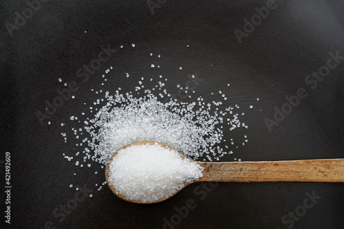 wooden spoon full of sugar crystals on a black plate,  top view photo