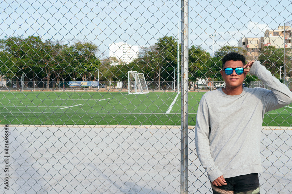 Fototapeta premium Urban young man wearing fashionable sunglasses near a fence. Attractive man enjoys the sun outdoors