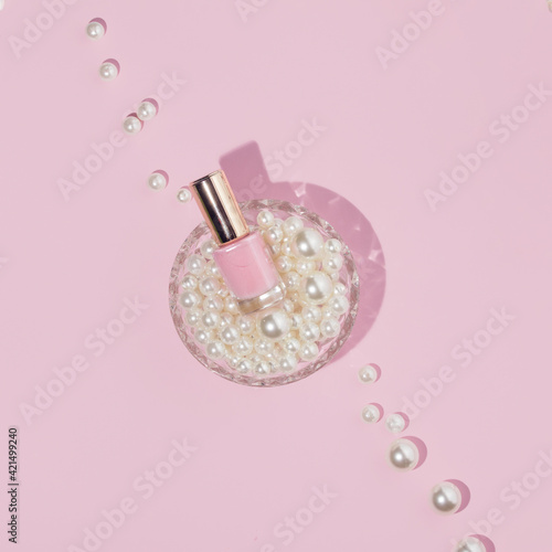 Romantic creative concept made with crystal jar with pearls and nail polish on blush pink background. Minimal flat lay. Vintage style aesthetic.