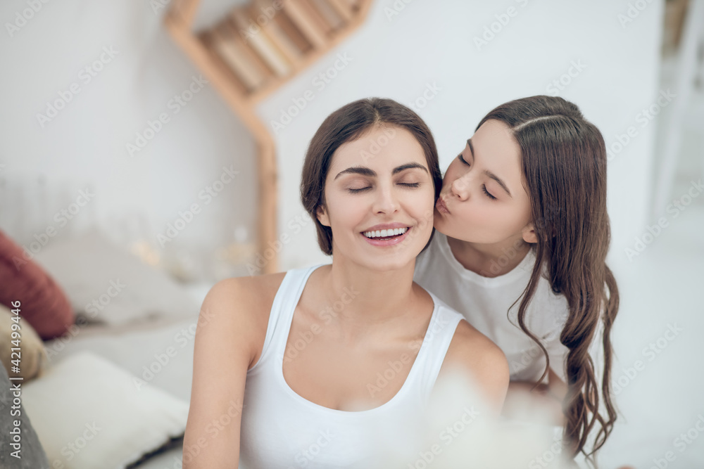 Teen daughter kissing happy mom with closed eyes Teen daughter kissing happy mom with closed eyes