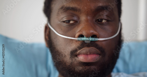 Close up of young african man patient with nasal cannula resting in bed at hospital photo