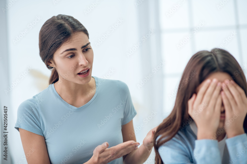 Attentive knowledgeable mother talking to turned away daughter Attentive knowledgeable mother talking to turned away daughter