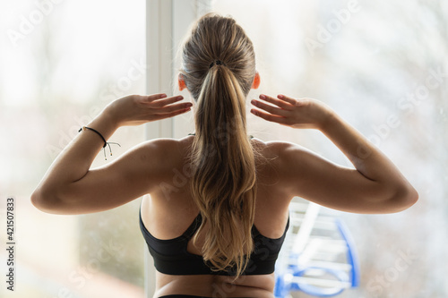 Young blonde caucasian woman stretching in front of the window. Home spring sport exercises. being on diet, Back view. Body positive workout.