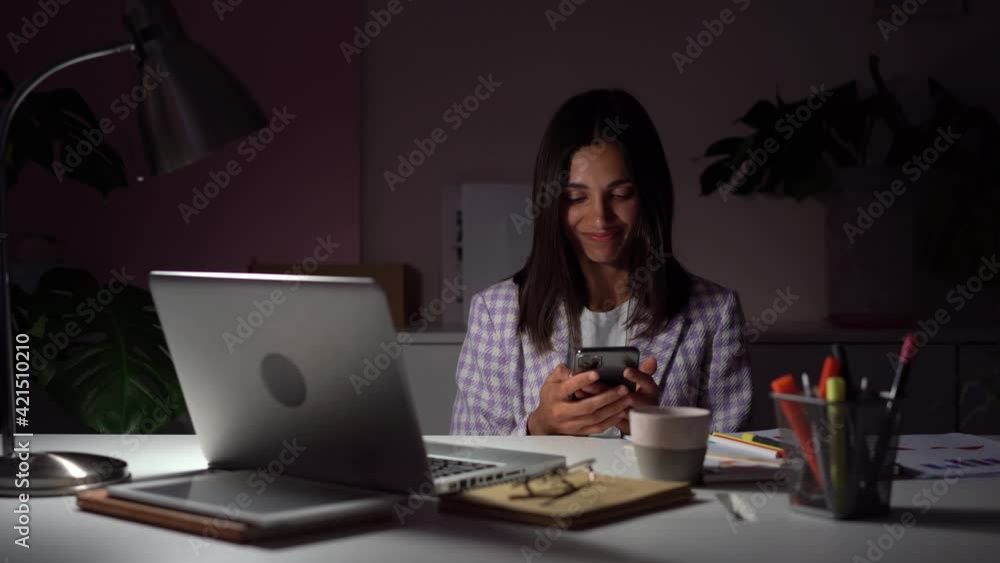 Indian mixed-race businesswoman browsing internet on phone at evening at work place Indian mixed-race businesswoman browsing internet on phone at evening at work place