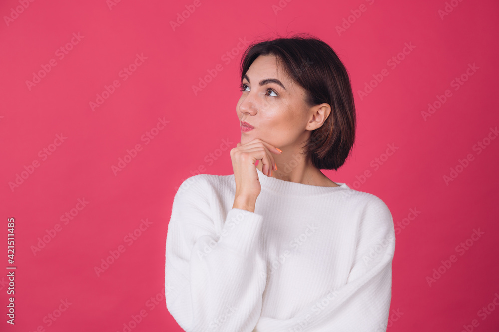Beautiful woman in casual white sweater on pink red background looks to the side thoughtfully with a sweet smile isolated copy space Beautiful woman in casual white sweater on pink red background looks to the side thoughtfully with a sweet smile isolated copy space