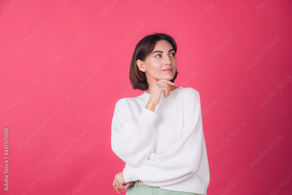 Beautiful woman in casual white sweater on pink red background looks to the side thoughtfully with a sweet smile isolated copy space Beautiful woman in casual white sweater on pink red background looks to the side thoughtfully with a sweet smile isolated copy space