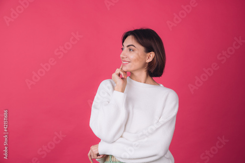Beautiful woman in casual white sweater on pink red background looks to the side thoughtfully with a sweet smile isolated copy space