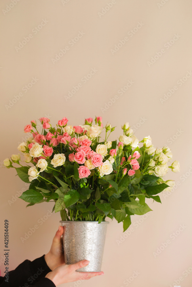 Bouquet of small pink and cream roses in a vase in female hands